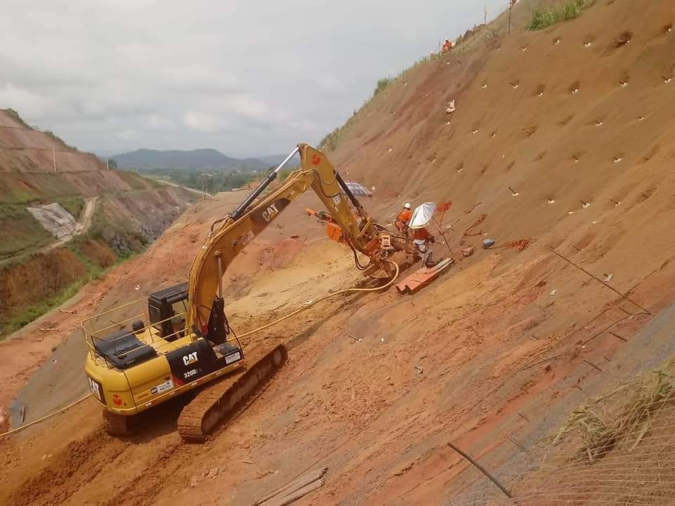 Escavadeira amarela trabalhando em talude de solo vermelho