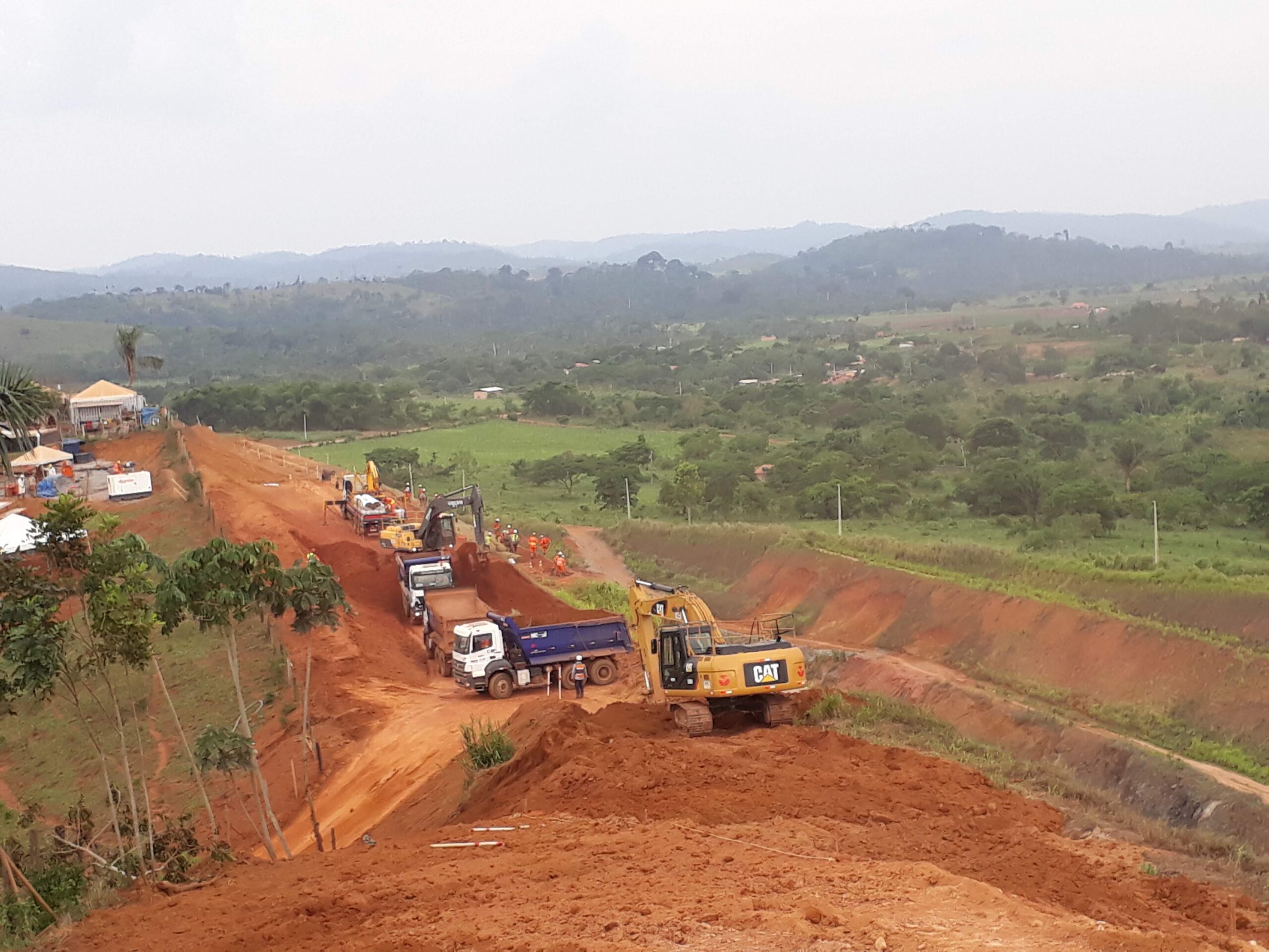 Obra viária em solo vermelho com escavadeira e caminhões